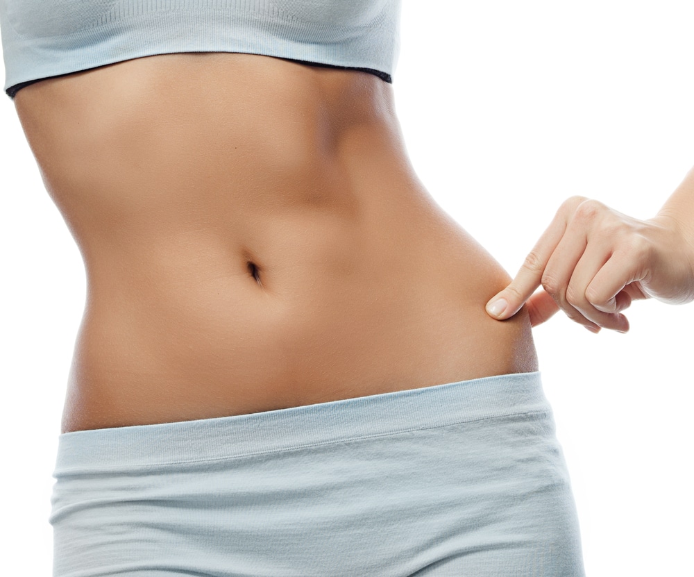 Close up of woman’s slim midsection as she pinches side after CoolSculpting treatment.